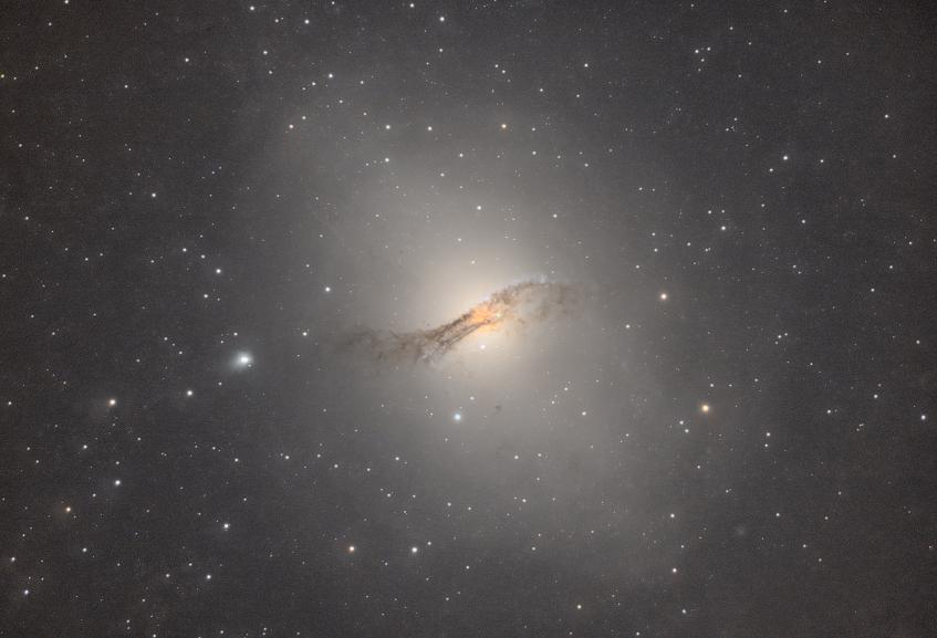A large bright oddly shaped galaxy with a dark dust band across it