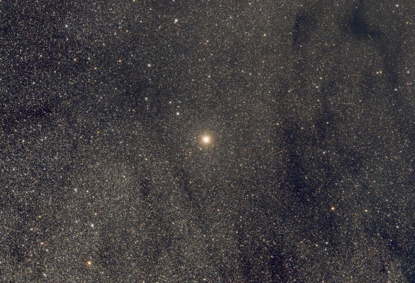 A bright red star on a background of dense faint stars and some dark dust sweeps.